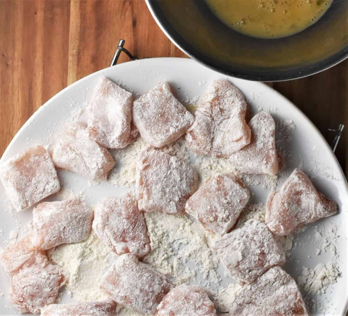 Coating chicken breast pieces in flour on top of plate.