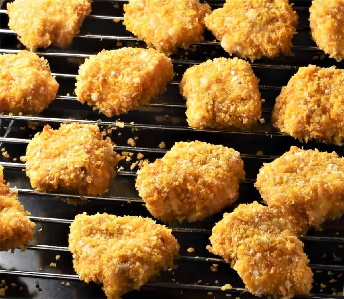 Side view of baked chicken nuggets with cornflakes on rack.