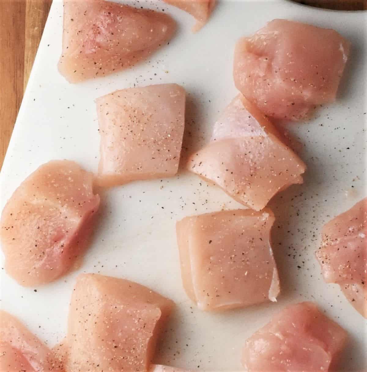 Cutting bite size chicken pieces on white board.