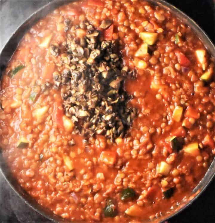 Top down view of lentil tomato sauce with chopped mushrooms in pan.