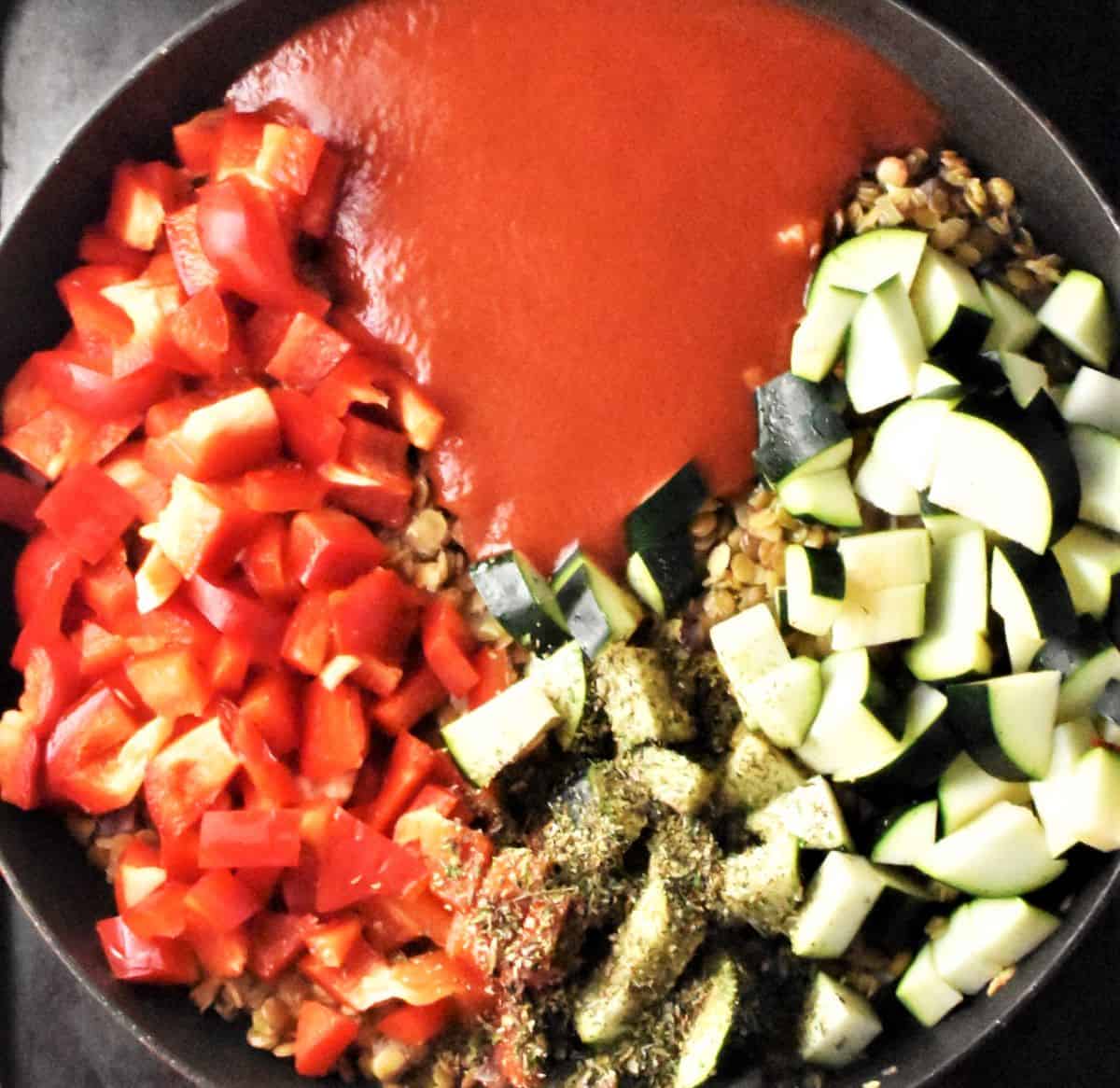 Cubed zucchini, red pepper and passata in pan.