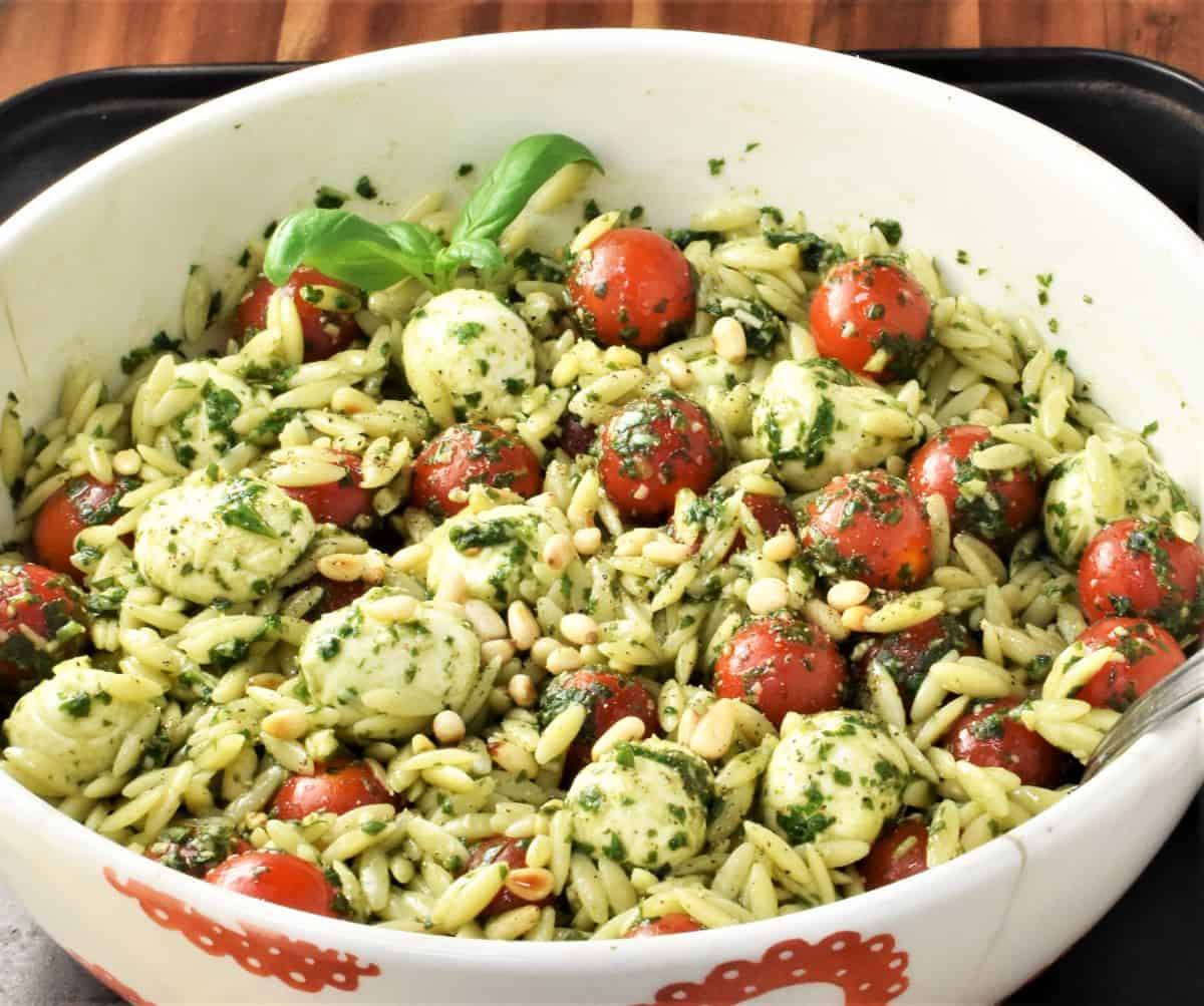 Close-up view of pasta with pesto and tomatoes in white bowl.