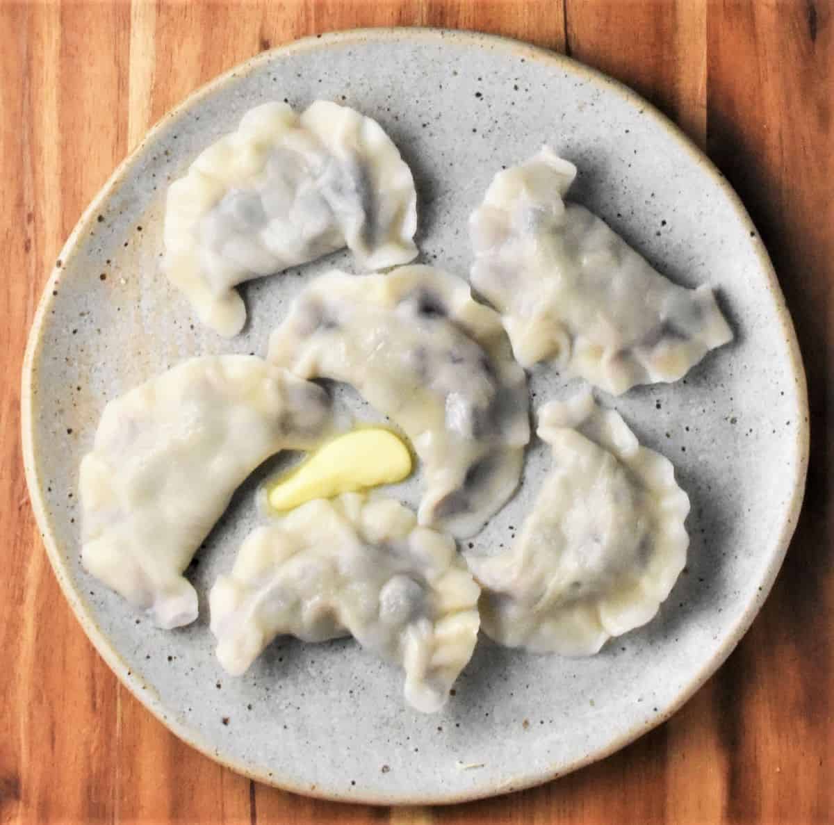 Just boiled Polish blueberry dumplings on top of grey plate with butter.