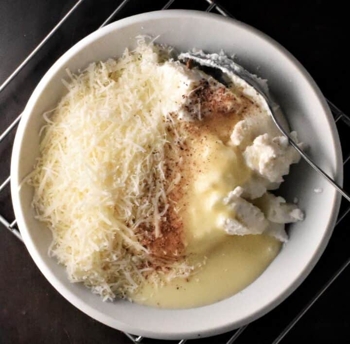 Ricotta with creamy sauce and grated cheese in white bowl.