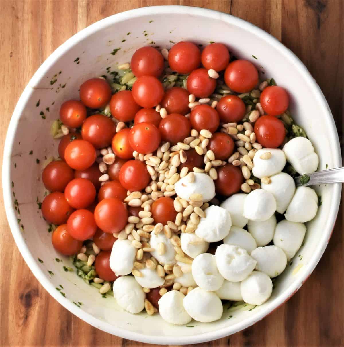 Assembling caprese pesto pasta salad in white bowl.