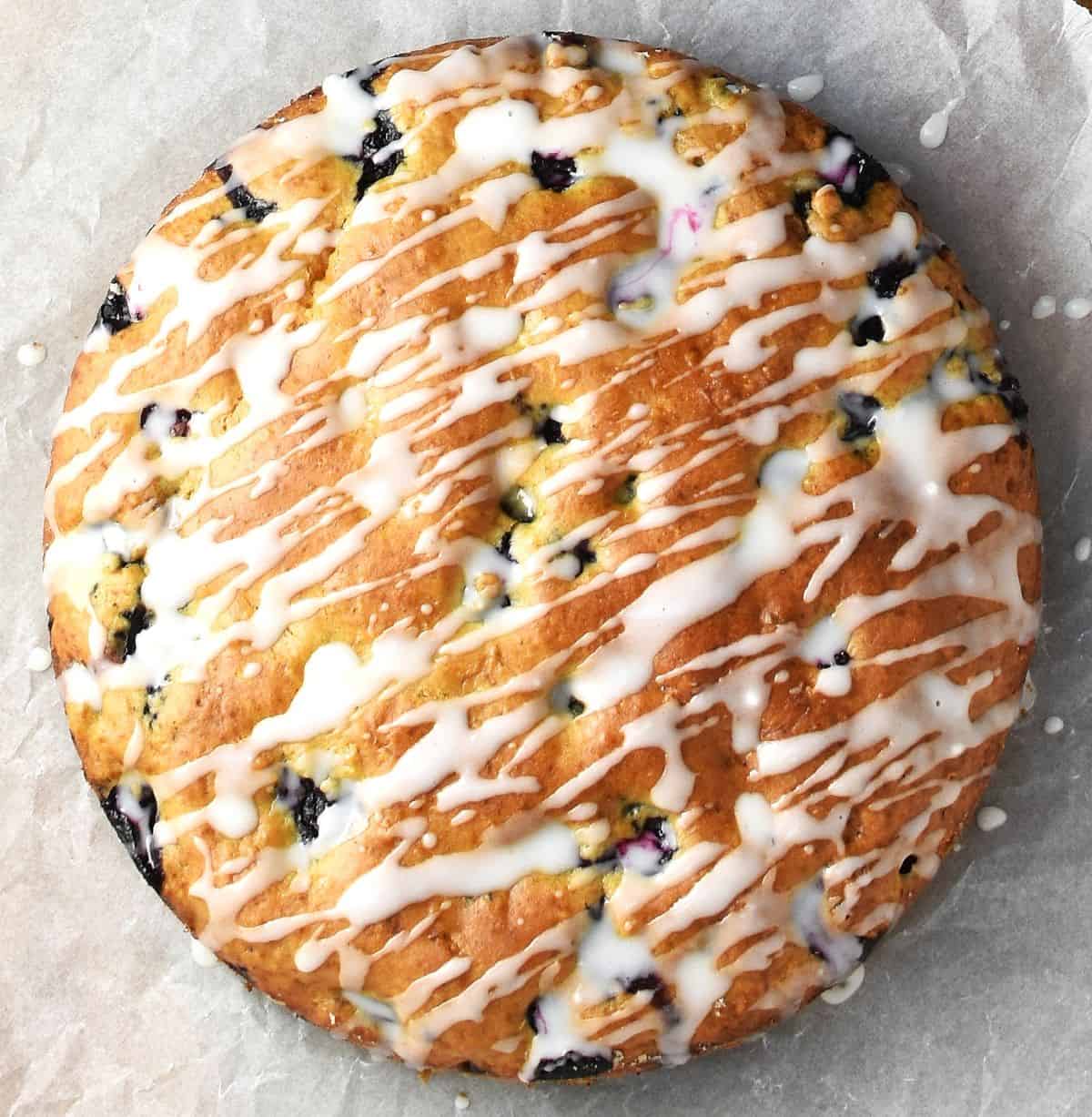 Top down view of blueberry breakfast muffin cake with lemon drizzle on parchment.