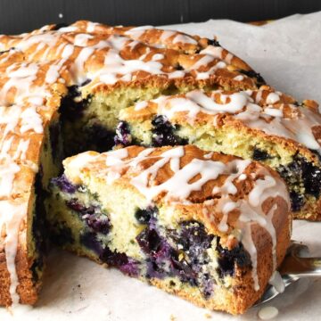 Side view of simple blueberry cake slice with cake in background on top of parchment.