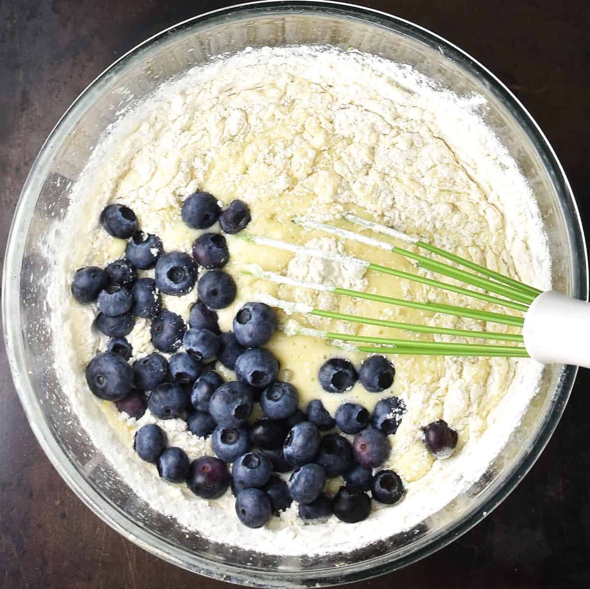 Top down view of blueberries with flour and wet mixture in glass bowl with whisk.