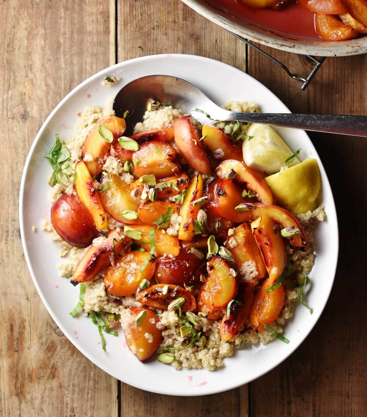 Quinoa salad with peaches, lemon wedges and nuts on top of white plate with large spoon.