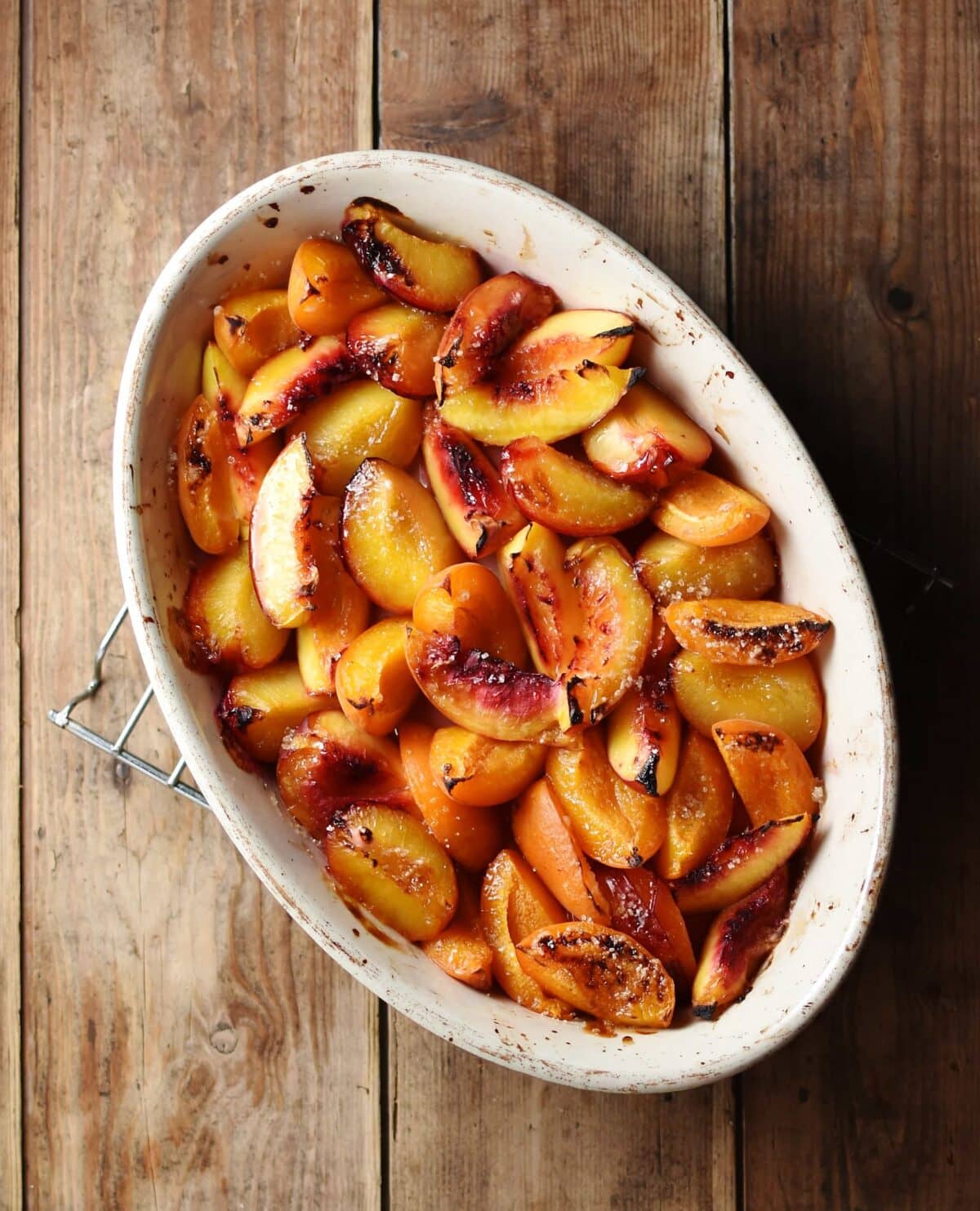 Top down view of roasted peach wedges inside white oval dish.