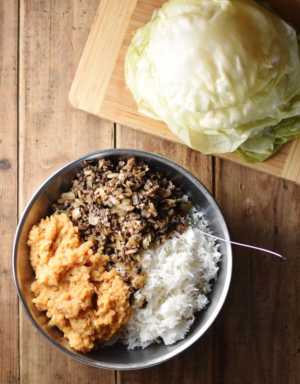 Top down view of rice, lentils and mushrooms in bowl, with cabbage leaves on top of cutting board.