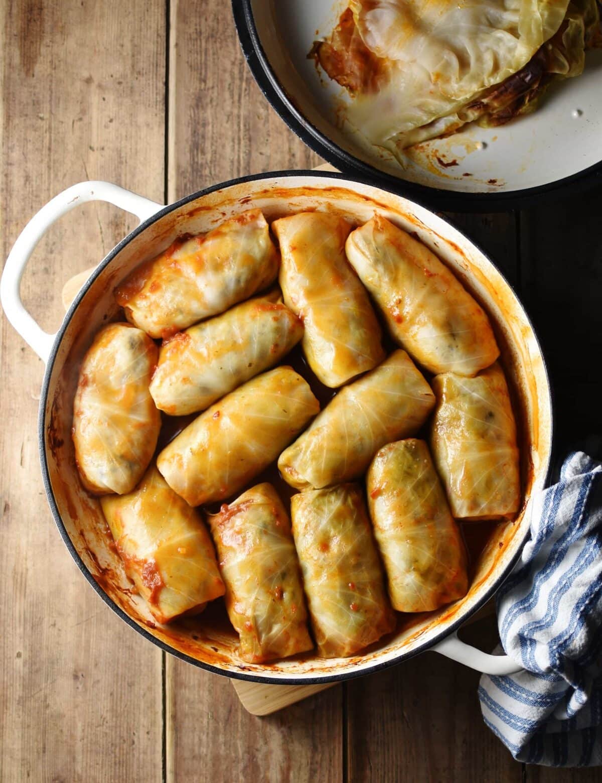 Top down view of cabbage rolls in large white dish with lid in top right corner and blue-and-white cloth in bottom right.