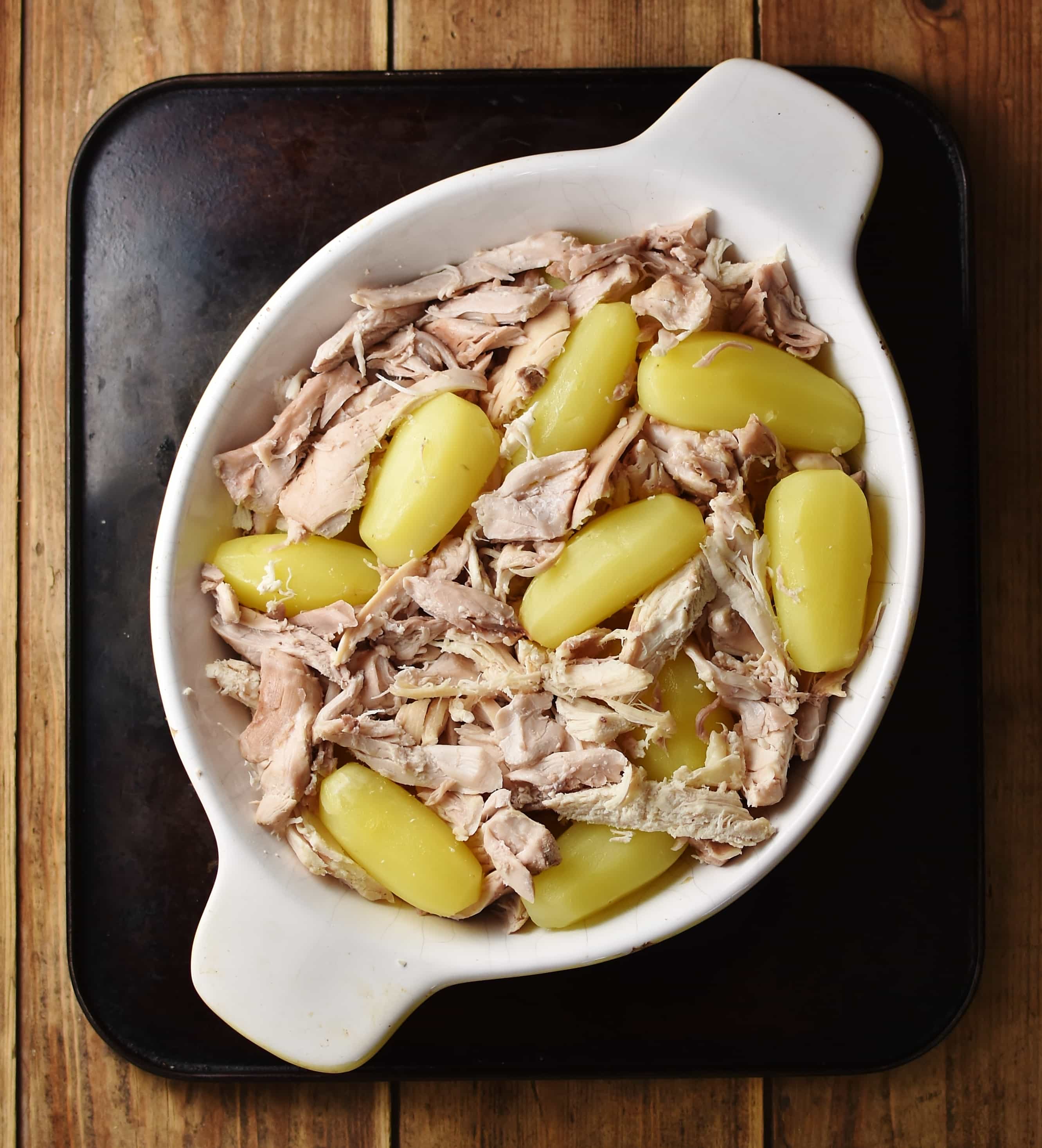 Peeled potatoes and chicken pieces inside white oval dish.
