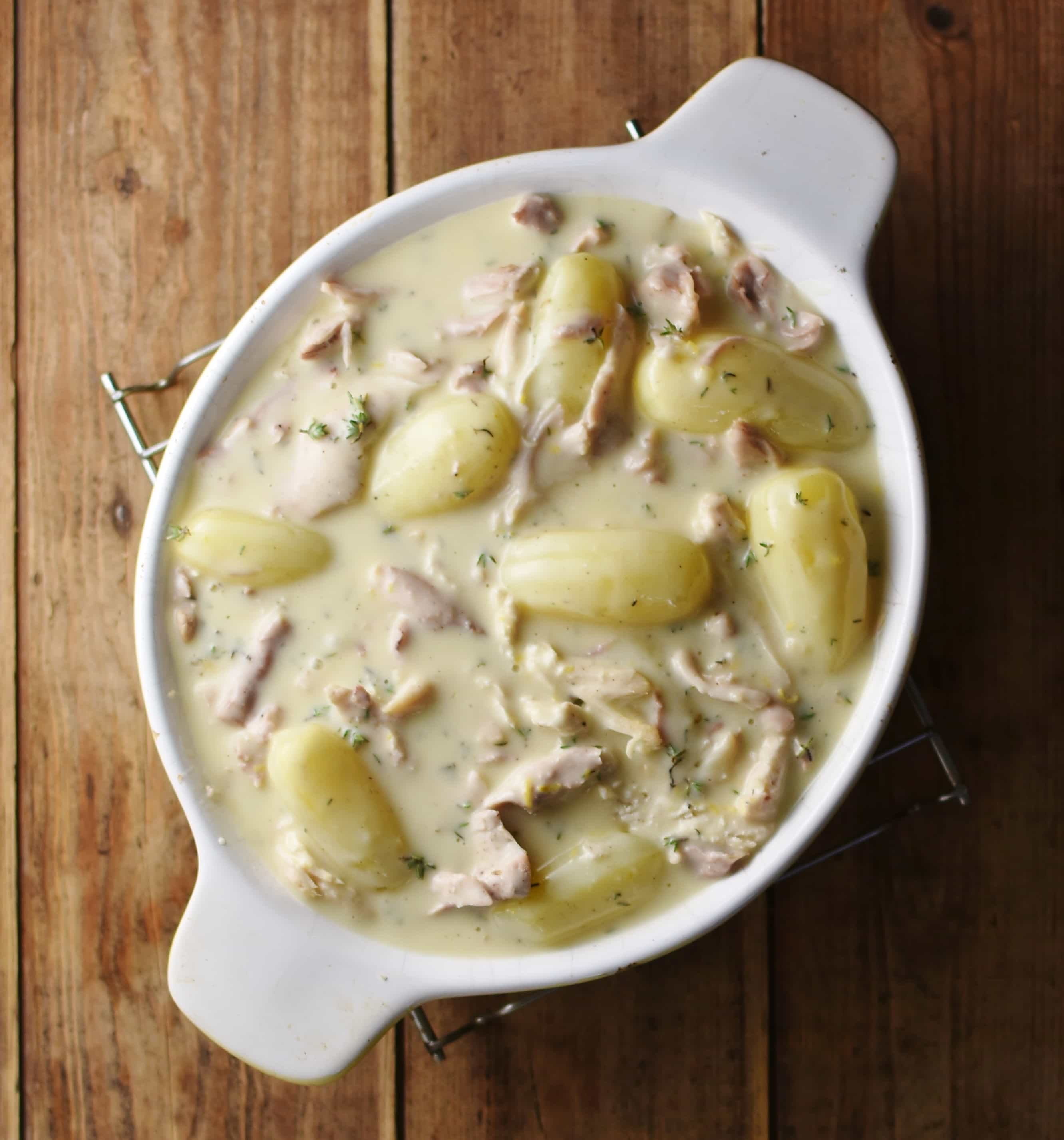 Potatoes and chicken pieces in creamy sauce inside white oval dish.