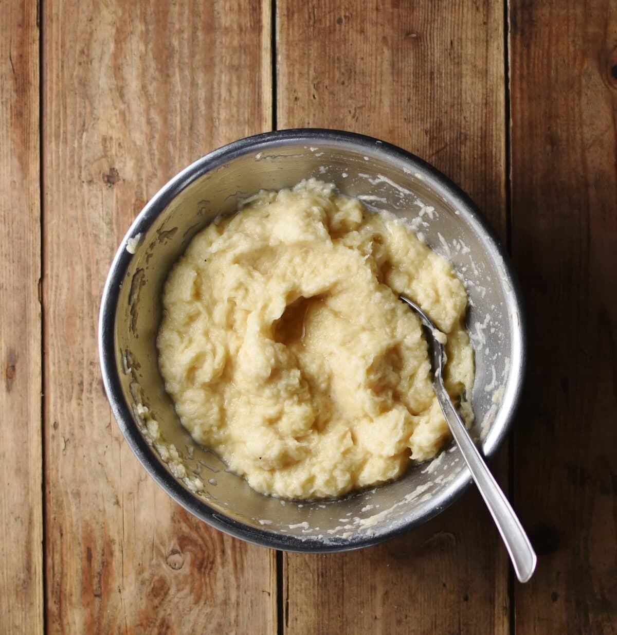 Potato pancake batter with spoon inside metal bowl.