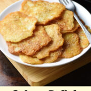 Crispy pancakes on top of white plate with fork, sour cream with spoon in white dish and pancakes in pan in background.