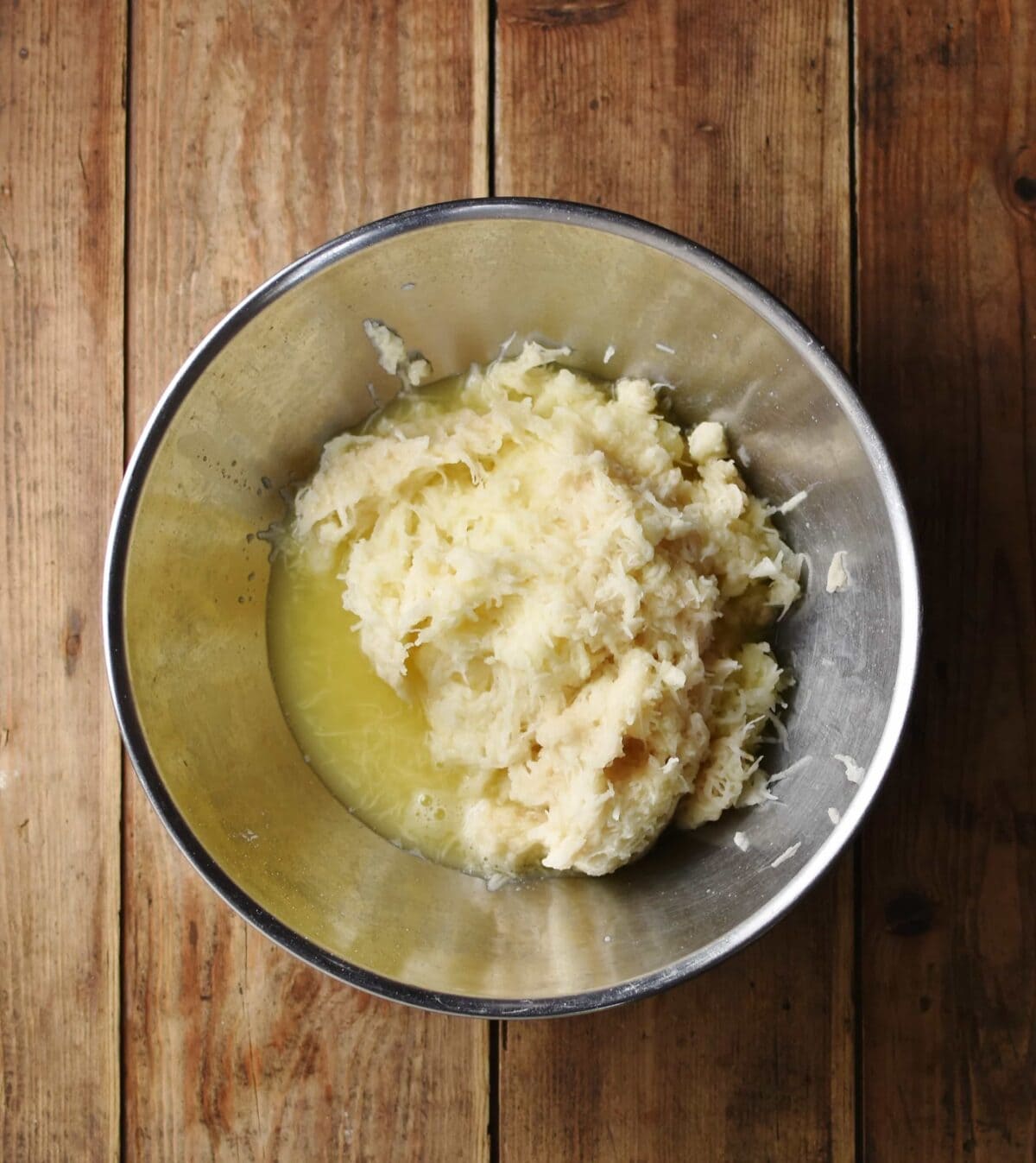 Grated potato mixture in metal bowl.