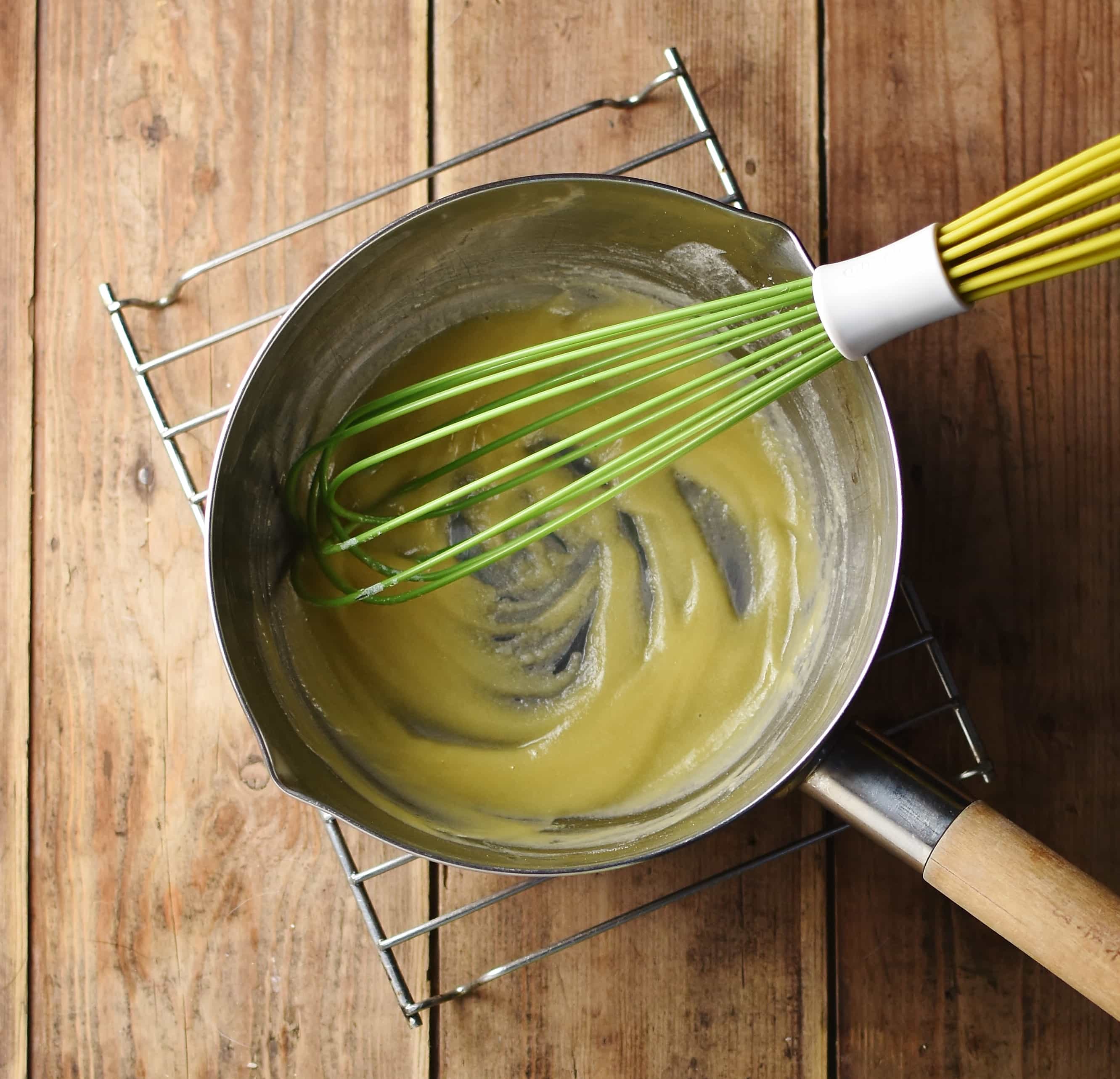 Roux inside saucepan with green whisk on top of cooling rack.