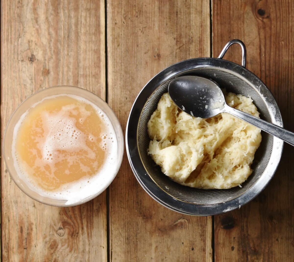 Potato mixture in strainer with spoon and water from potatoes in small bowl.