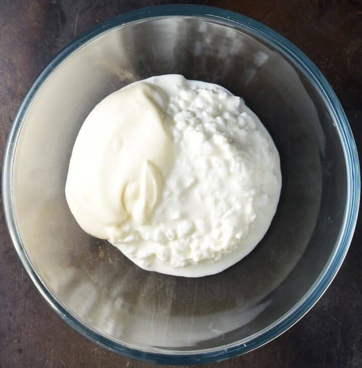 Top down view of cottage cheese and mayo in glass bowl.