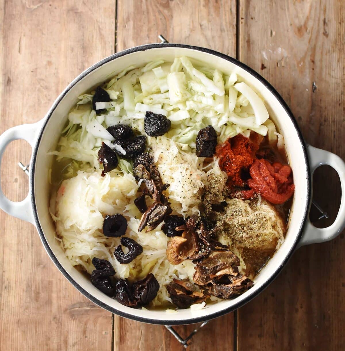 Sauerkraut, chopped cabbage, prunes, spices and dried mushrooms in large white pot.