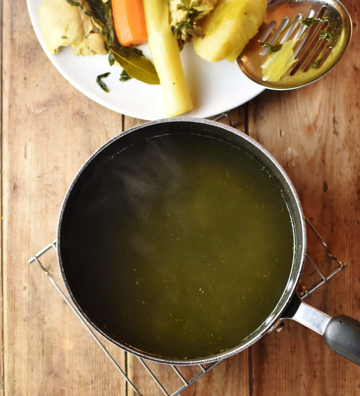 Clear soup in large pot, with cooked chicken and vegetables on white plate at the top.