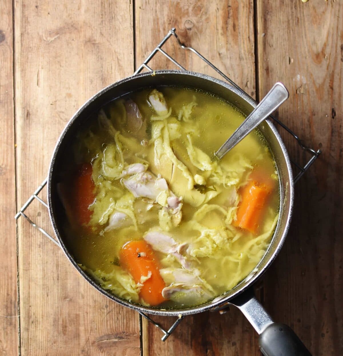 Egg drop noodle chicken soup with carrots and spoon in large pot.