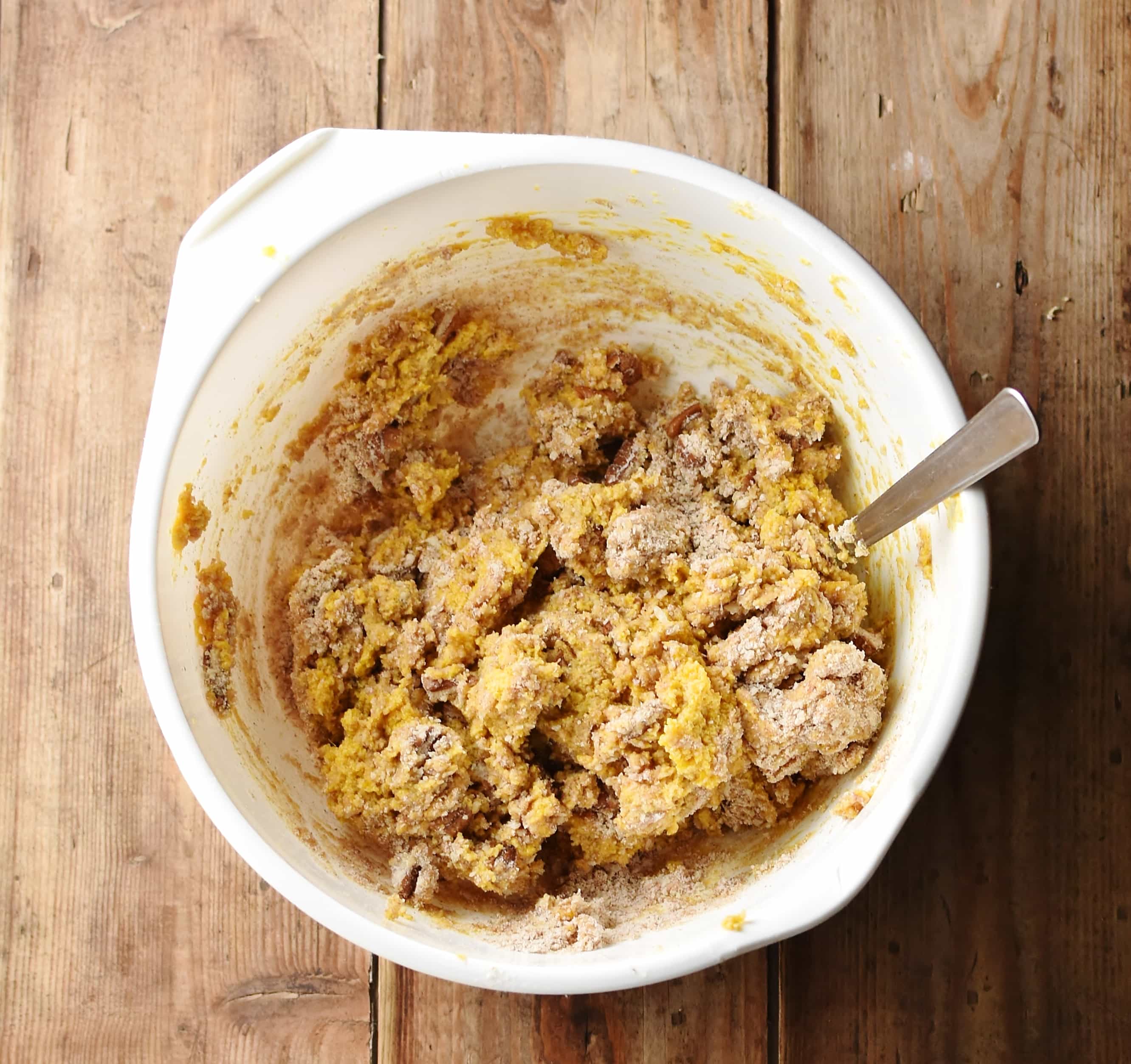 Pumpkin cookie batter with spoon in large white bowl.
