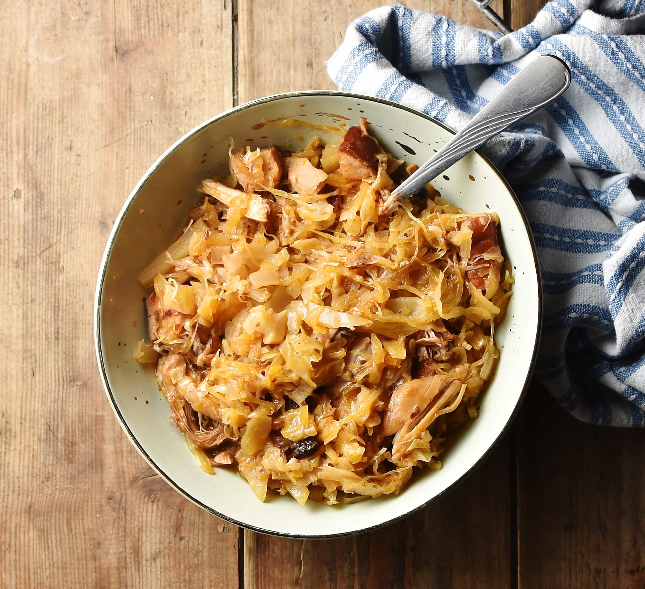 Bigos with spoon in green bowl with stripy blue-and-white cloth to the right.