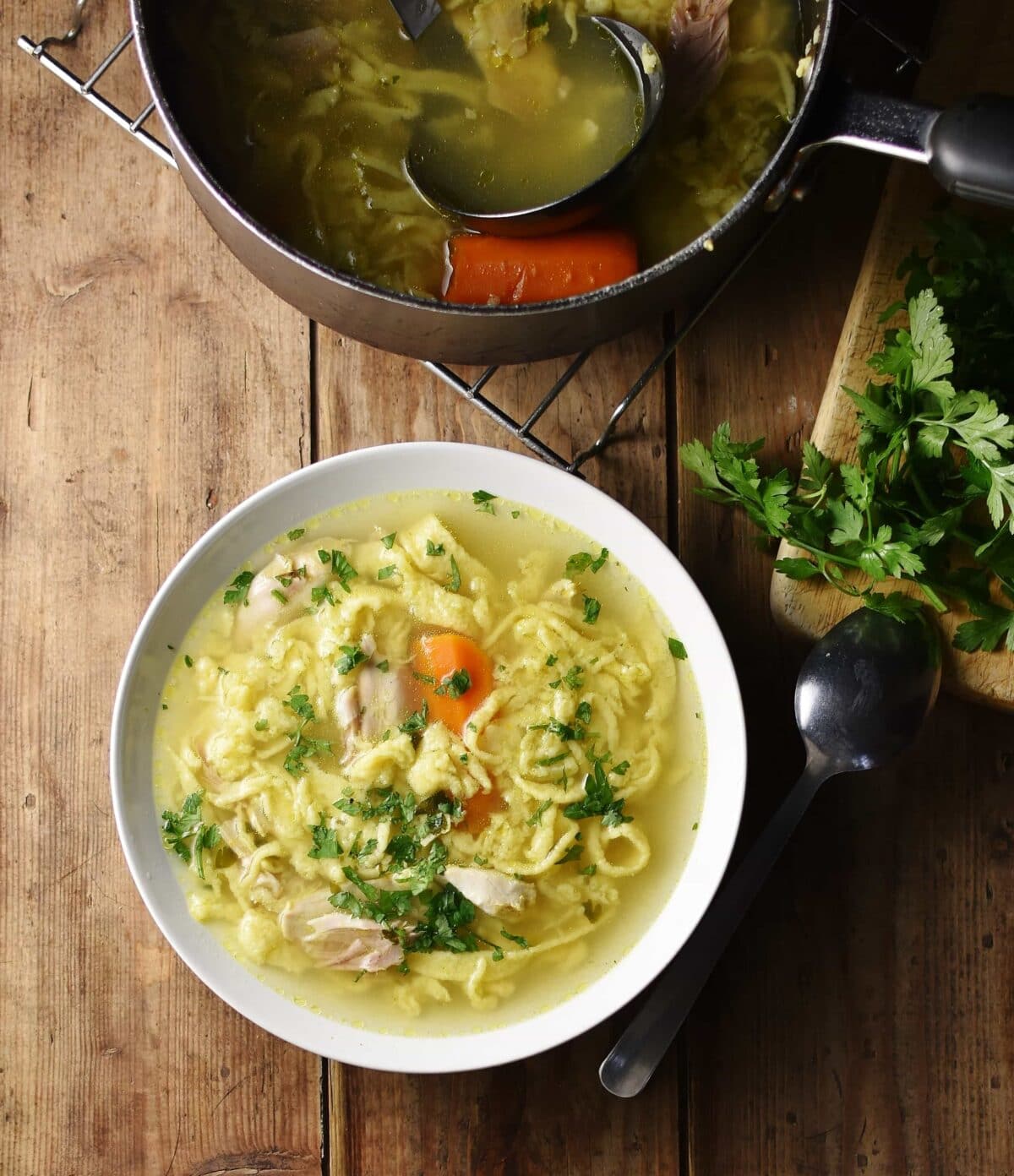 Egg drop noodles chicken soup with parsley in white bowl, with spoon and parsley to the right and soup in top at the top.