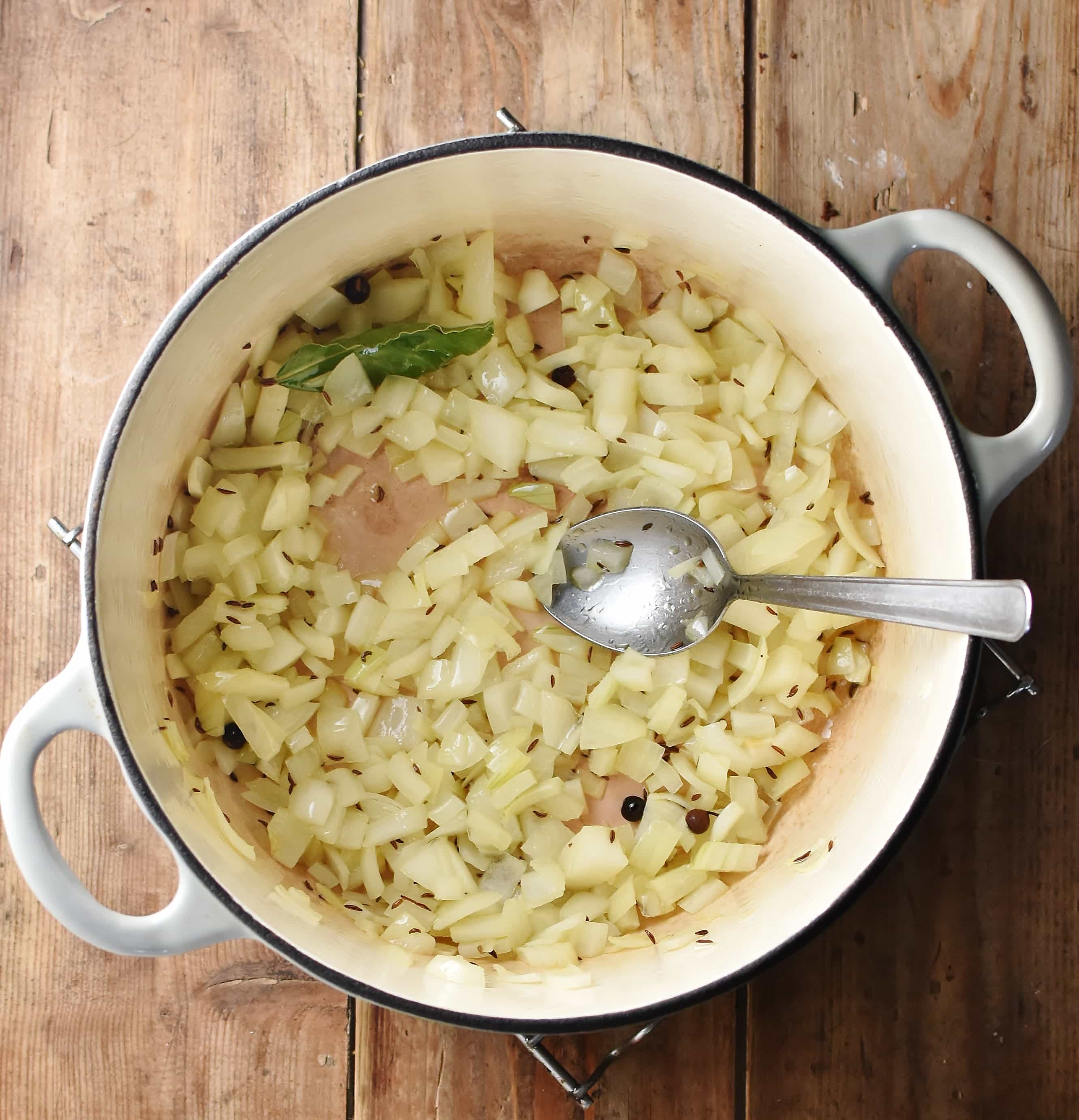 Chopped onions in large white pot with spoon.