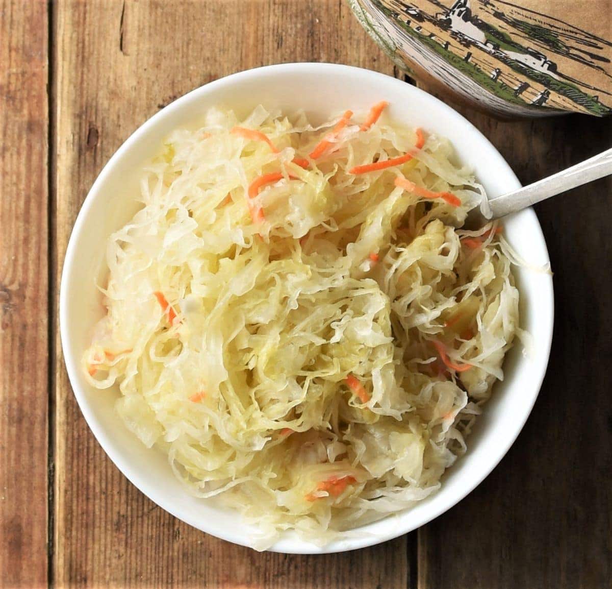 Top down view of sauerkraut in white bowl with spoon.