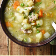 Chunky chicken and vegetable soup with spoon in purple bowl wrapped in green cloth.