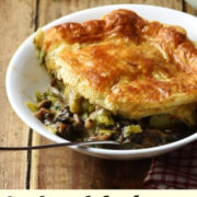 Side view of mushroom and leek pie with golden brown pastry in white bowl with fork, with pie dish and mushrooms in background.