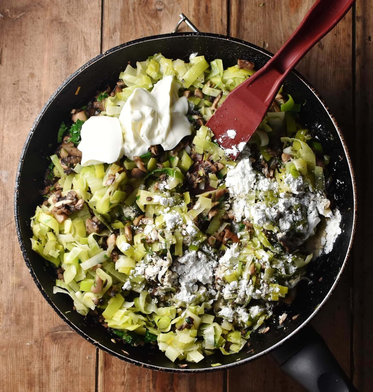 Chopped leeks, mushrooms, yogurt and flour in large skillet with red spatula.