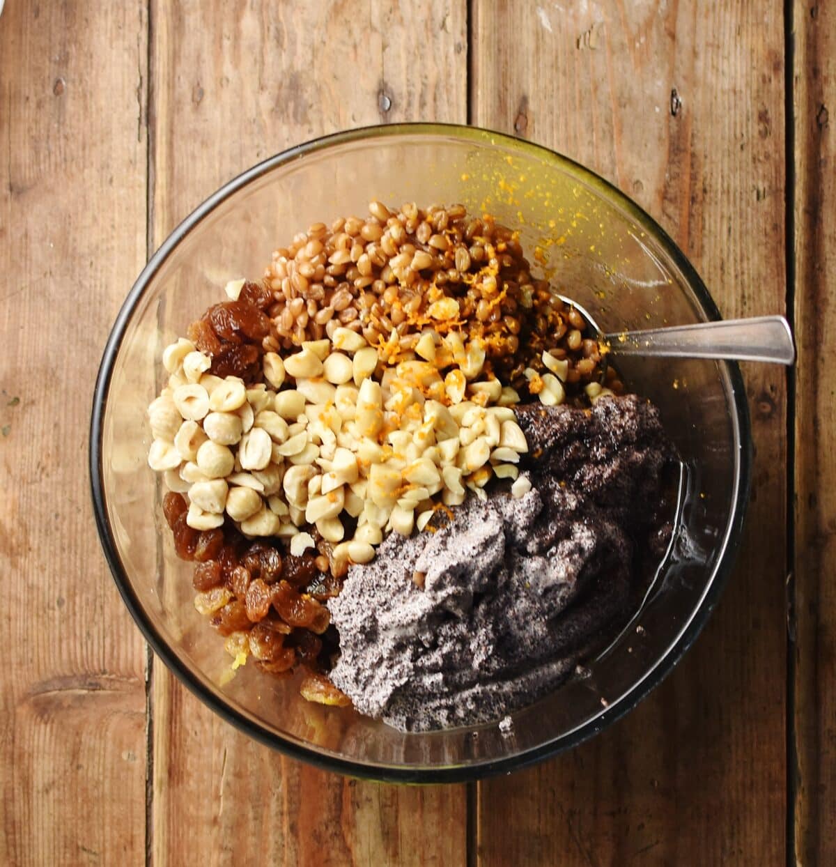 Kutia ingredients including wheat berries, creamy poppy seed mixture, raisins and nuts in mixing bowl with spoon.