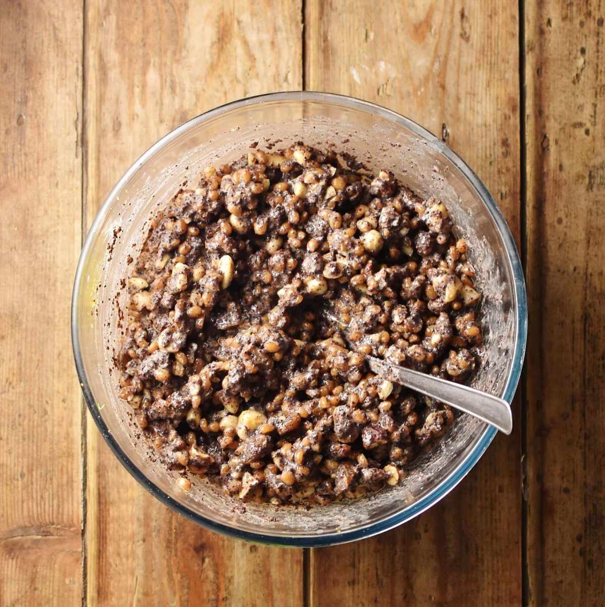 Wheat, poppy seed, nut and raisin mixture in mixing bowl with spoon.