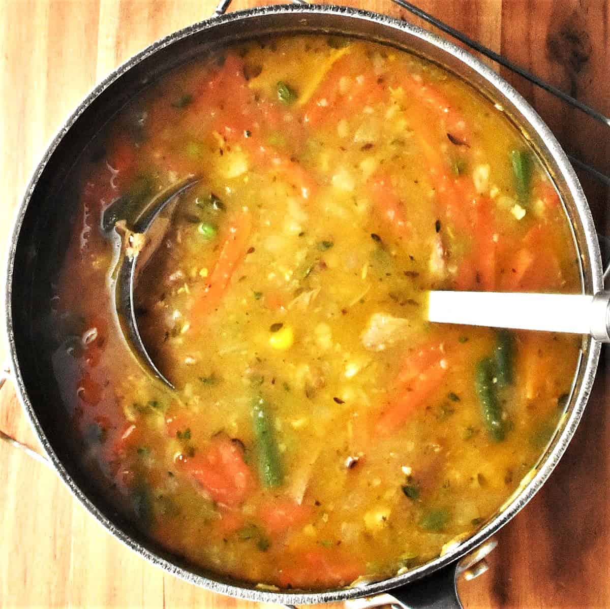 Top down view of chunky vegetable turkey soup in pot with ladle.