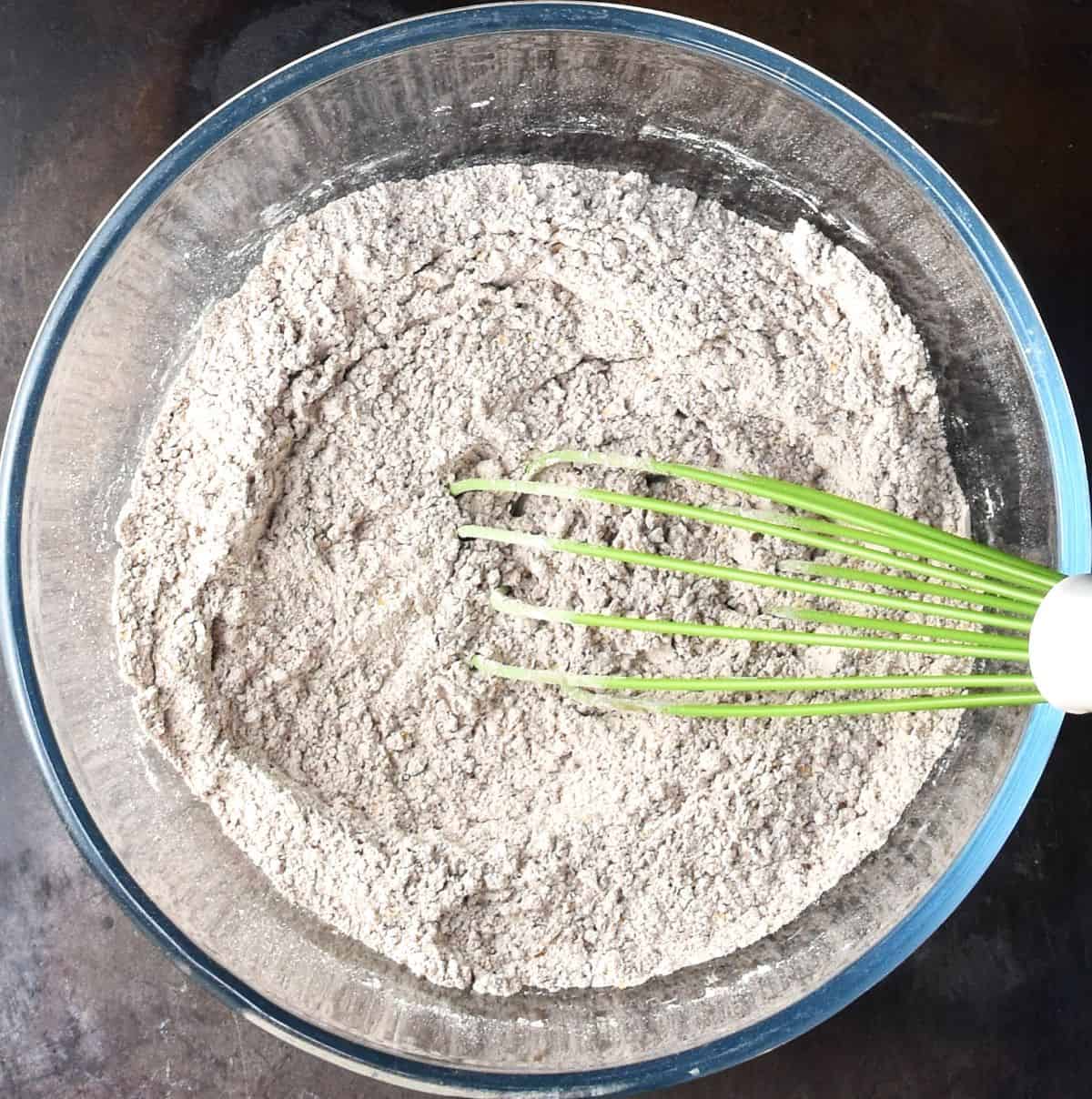 Dry mixture for gingerbread muffins in glass bowl with green whisk.