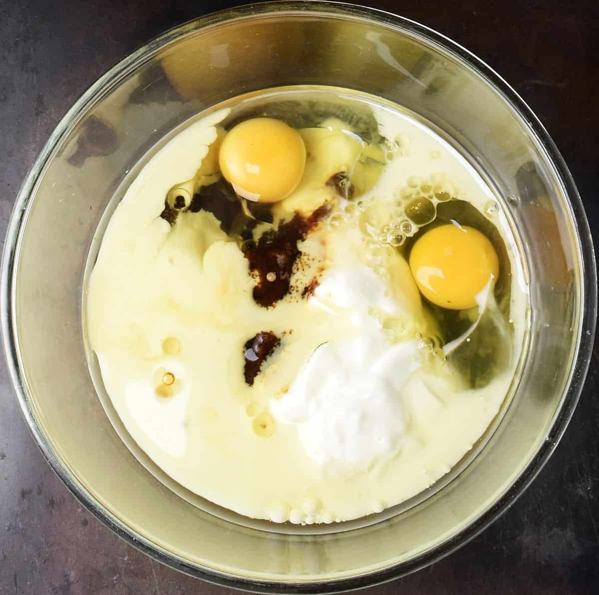Top down view of 2 raw eggs, milk and sugar in glass bowl.