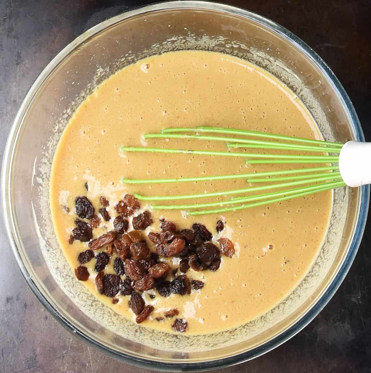 Gingerbread muffin wet mixture with raisins in bowl with whisk.