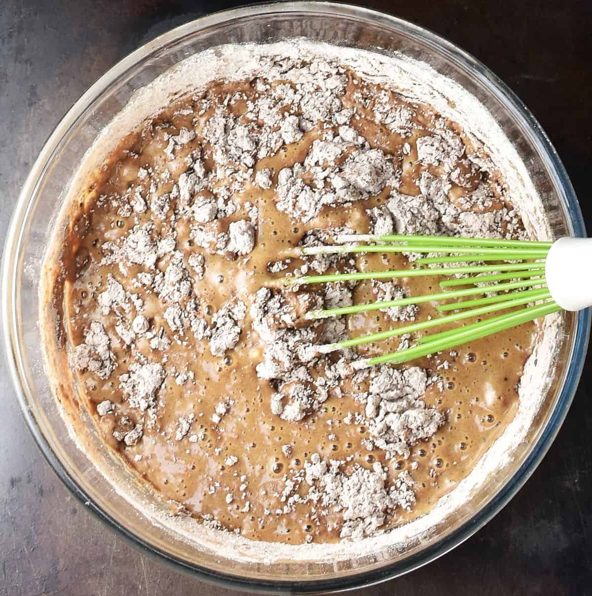 Gingerbread muffin batter with flour visible in bowl with whisk.