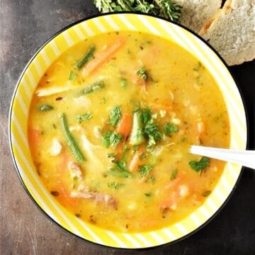 Top down view of turkey vegetable soup in yellow bowl with spoon.