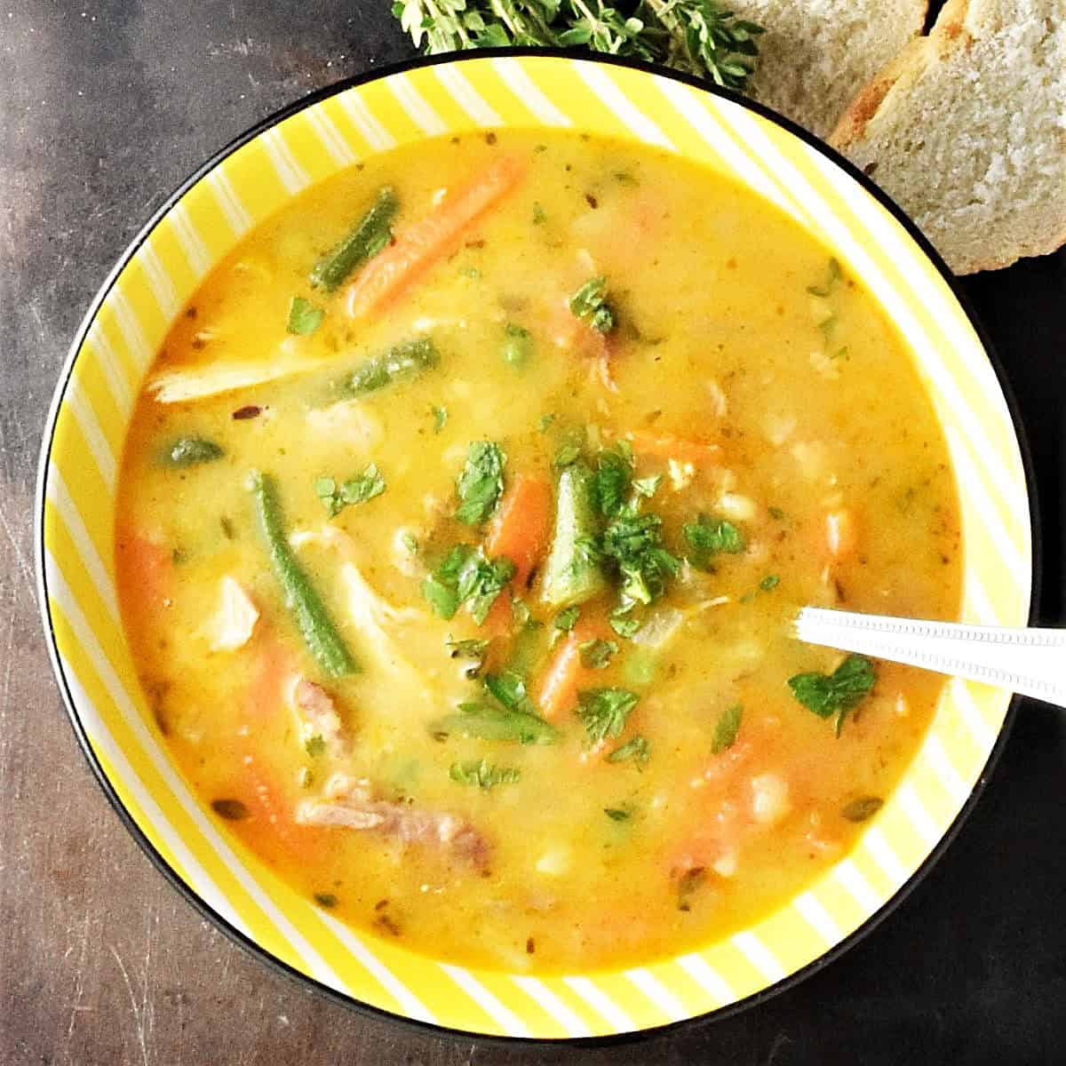 Top down view of turkey vegetable soup in yellow bowl with spoon.