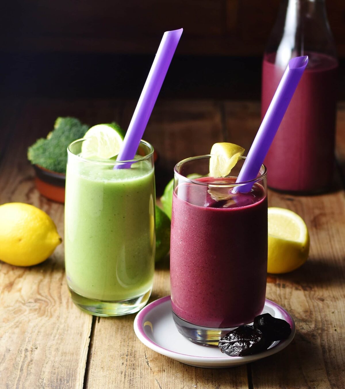 Purple and green broccoli smoothies with purple straws and lemon in background.