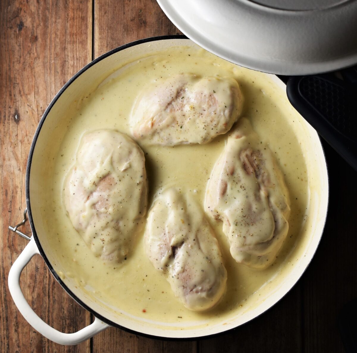 4 chicken breasts in creamy sauce in large shallow white pan with lid in top right.