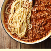Spaghetti bolognese in large shallow white dish with fork and grated cheese in small dish in background.