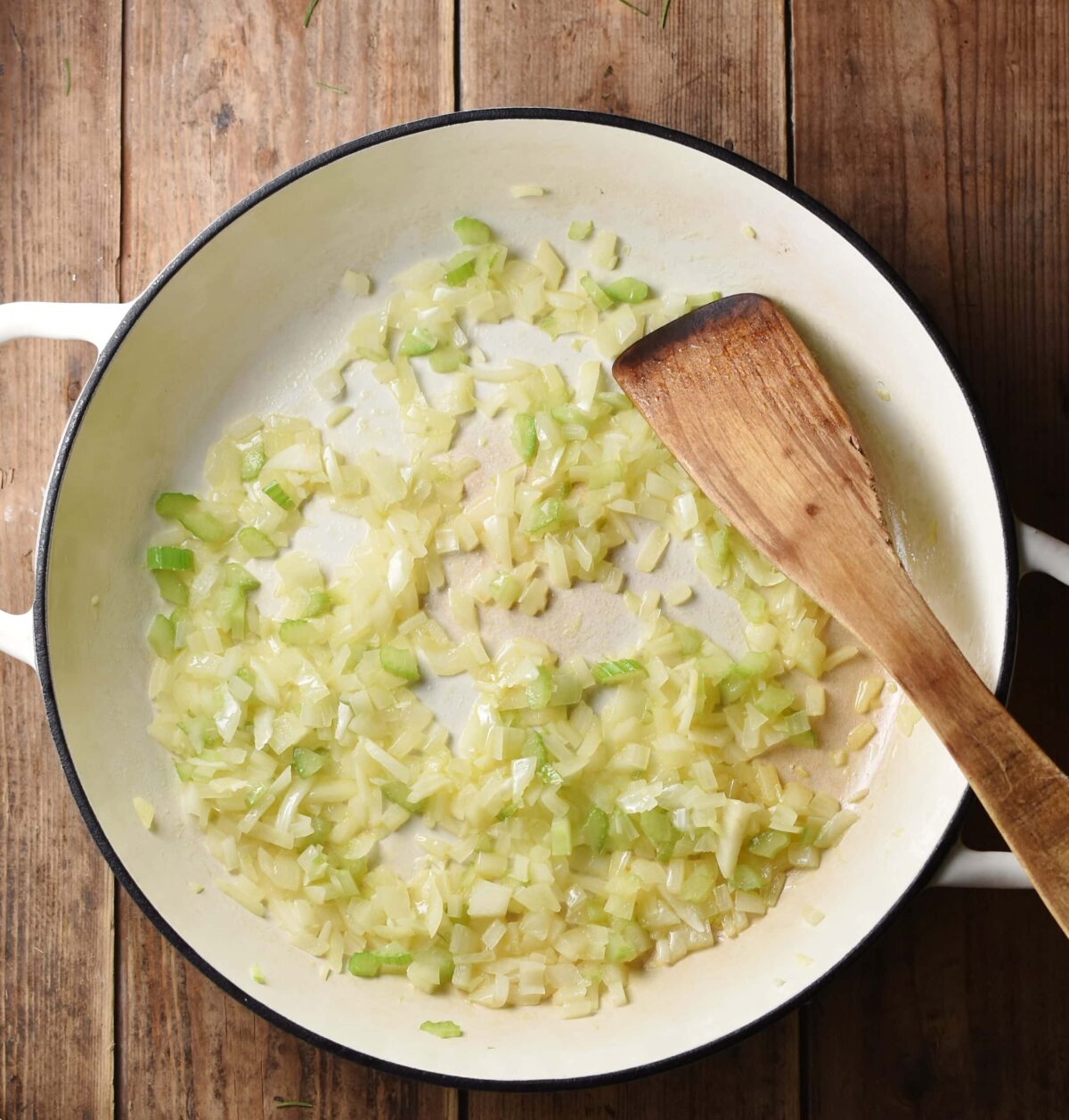 Chopped onions and celery in large white shallow dish with wooden spatula.