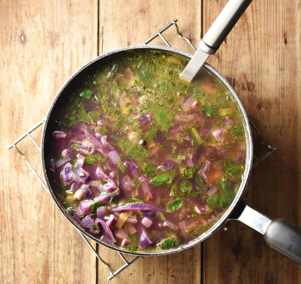 Red vegetable soup with herbs in large pot with ladle on top of rack.