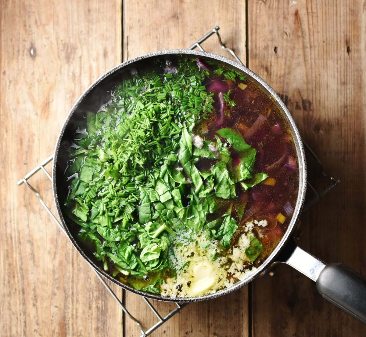 Red vegetable soup with fresh herbs and butter in large pot on top of rack.